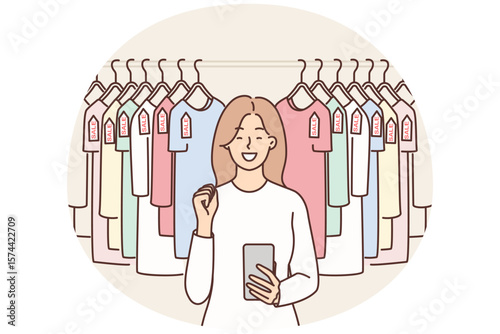 Woman with phone near hanger with T-shirts rejoices sale and opportunity to buy clothes at discounts