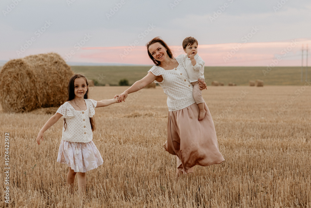 Mother and her two children: son and daughter in a field of haystacks in the summer at sunset. motherhood, mother's day Mother and her two children: son and daughter in a field of haystacks in the summer at sunset. motherhood, mother's day