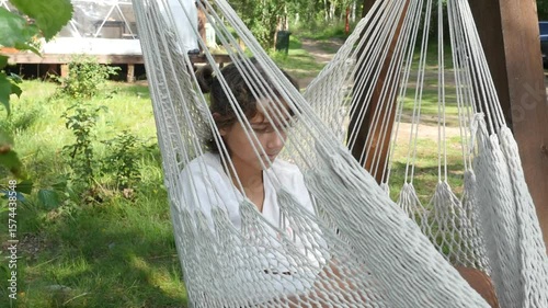 Girl relaxing in hammock.  View of cute teenage girl in white t-shirt swinging in hammock at forest camping.  Teenager using smartphone.