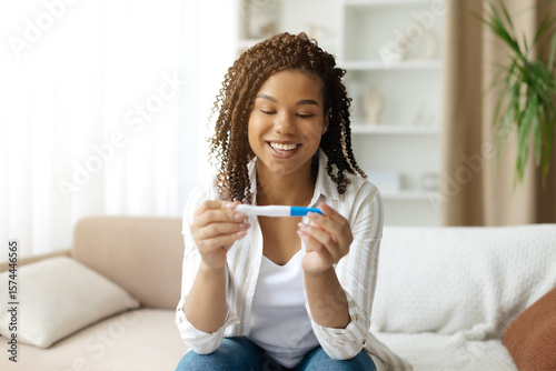 Tableau sur toile Happy black woman looking at positive pregnancy test at home