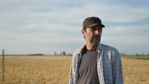 Male farmer standing in ripe wheat field and looking over the harvest ready crops at the horizon and sunny sky, 4K