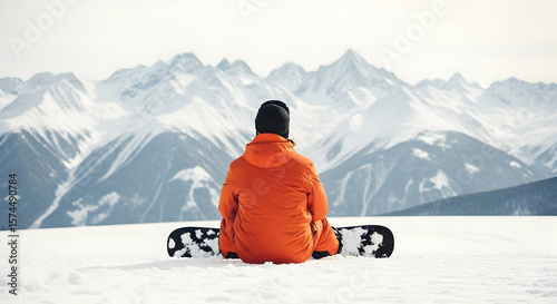 Person sitting on snowboard facing mountain range