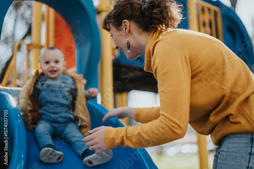 A mother helps her young child on a slide at a brightly colored playground, capturing a moment of excitement and bonding in a playful outdoor environment.