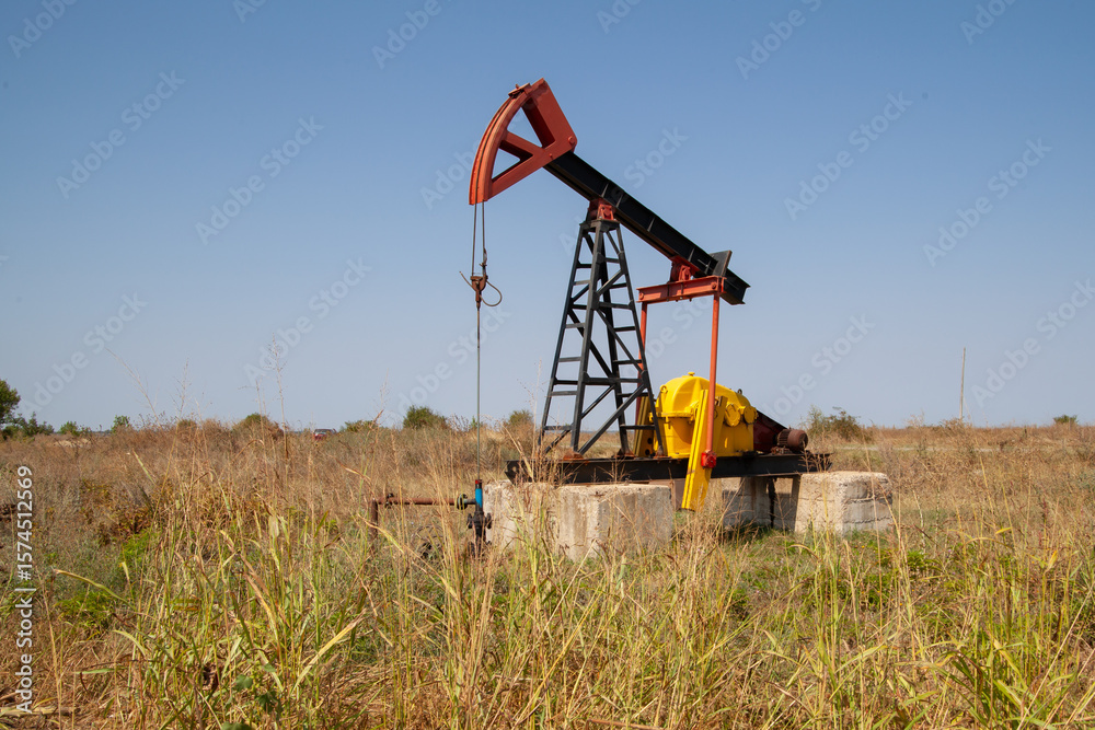 Industrial oil pump jack operating in a dry, grassy field. Onshore derrick for crude oil and gas extraction, representing the fossil fuel and petroleum industry. Industrial oil pump jack operating in a dry, grassy field. Onshore derrick for crude oil and gas extraction, representing the fossil fuel and petroleum industry.