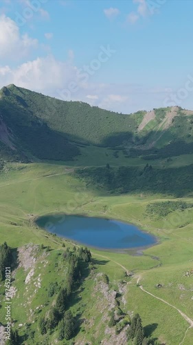 Aerial landscape revealing pristine blue lake surrounded by verdant valleys, rolling hills, vibrant azure sky featuring soft white cloud formations