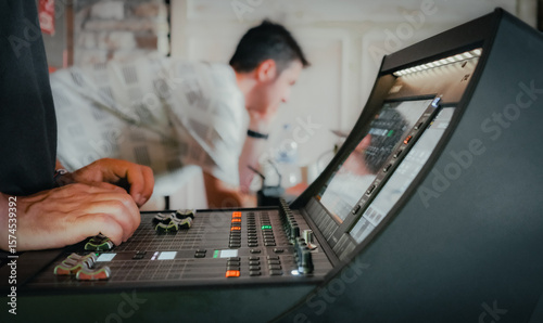 Two audiovisual engineers working together on a live event in a room. In the foreground, one of them's hands working on the audio mixer.