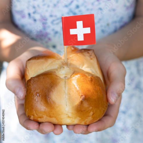 Swiss traditional August bread bun with a swiss flag in child hands, square format.