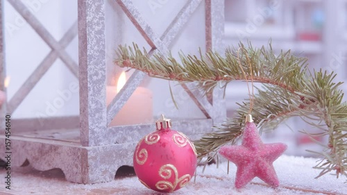 Christmas tree decoration, soft flame first Advent candle flickers inside garden lantern with snow gently falling in background for wintery feel, cozy Christmas scene
