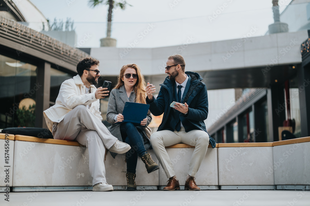 Fototapeta premium Business people are collaborate on a project while sitting in an outdoor. The group appears engaged, using devices and documents, reflecting teamwork, creativity, and a productive collaboration.