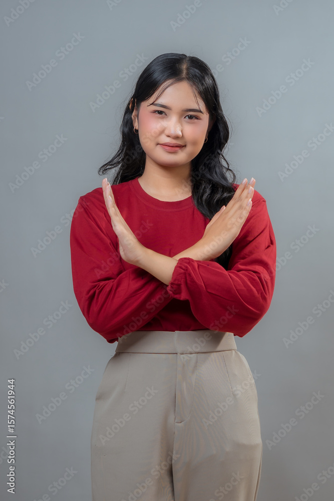 Obraz premium Young Indonesian woman wearing a red top and beige pants, crossing her arms in a 