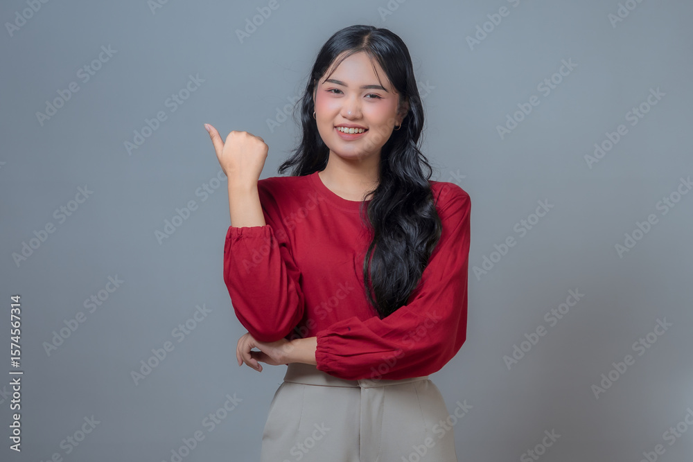 Smiling Indonesian woman in a red shirt and beige pants, giving a thumbs-up gesture with her right hand. A confident and positive body language in a studio with a gray background. Smiling Indonesian woman in a red shirt and beige pants, giving a thumbs-up gesture with her right hand. A confident and positive body language in a studio with a gray background.