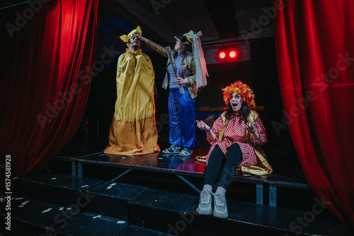 Two actors dressed in colorful costumes perform an engaging theatrical comedy scene on a decorated stage, capturing lively expressions and dramatic ambience under stage lights.