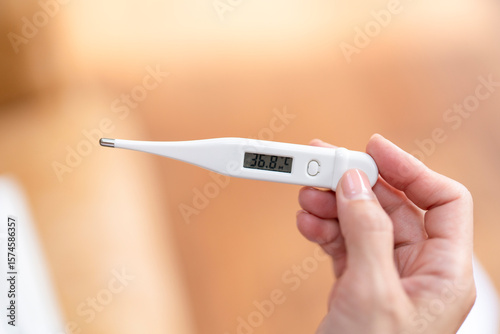 Person checks body temperature using a digital thermometer in a cozy indoor setting during a quiet afternoon