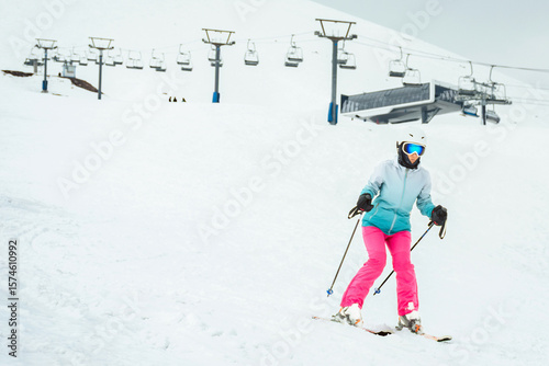 Canvas Print Woman skier in bright clothes skiing slowly on beginner slope with ski lift and