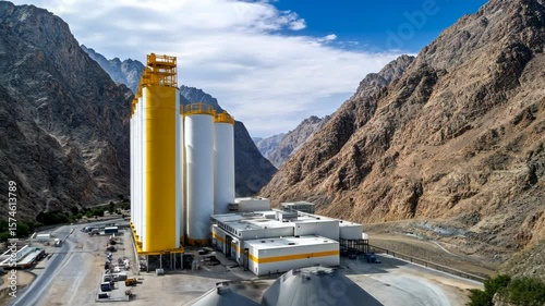 A cement facility operates in the mountains, featuring visible silos and machinery that blend industrial efforts with nature