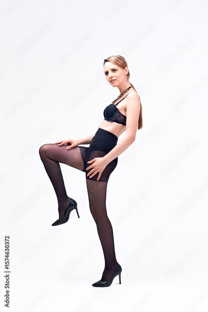Fototapeta premium A woman in a black bra and black stockings poses for the camera. She is wearing a necklace and high heels. The concept of elegance and sophistication.