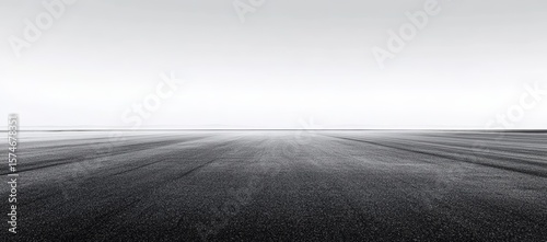 Vast empty asphalt road stretches to the horizon under a clear, bright sky, creating a minimalist and expansive landscape image.