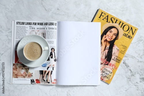 Trendy magazines and cup of coffee on white marble background, top view. Mockup for design
