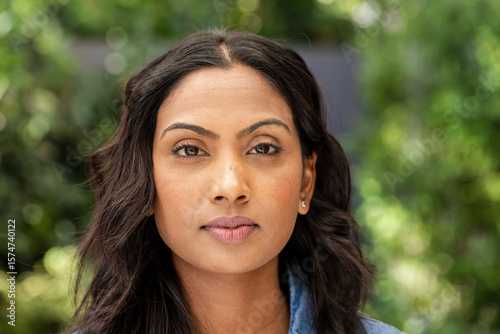 Indian woman wearing denim shirt posing in garden under soft sunlight, highlighting facial features