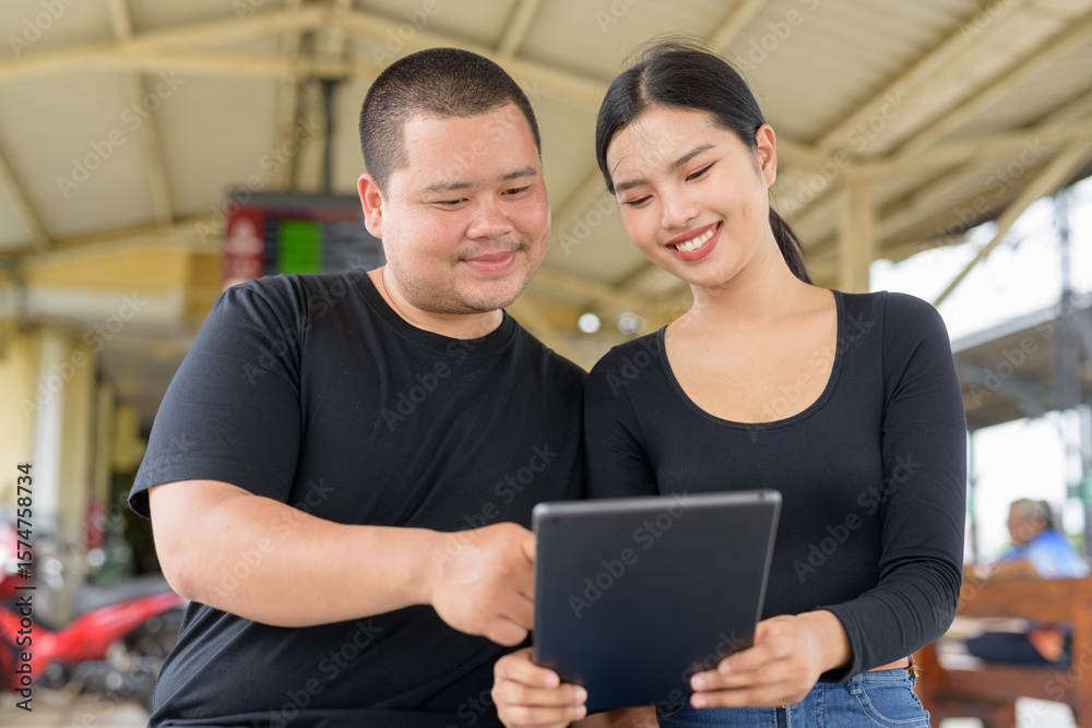Fototapeta premium Young couple in train station together using digital tablet computer