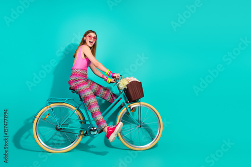Young girl riding a teal bicycle against a turquoise background showcasing vibrant summer fashion with retro accessories