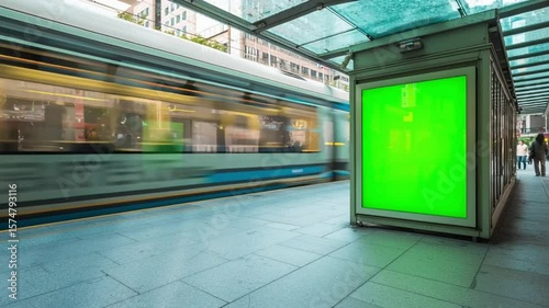 Blank green screen advertising billboard at a modern train station platform, with a blurred train in motion. Perfect for mockups and commercial displays in a public transit setting.

