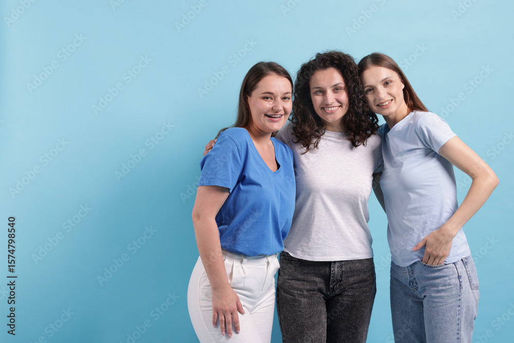 Fototapeta premium Three friends hugging on light blue background, space for text