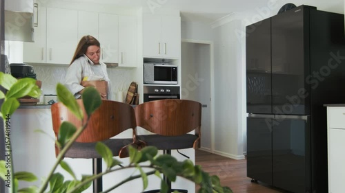 A woman is on the phone as she carries bags of fresh groceries into her home, showcasing a bright modern kitchen.