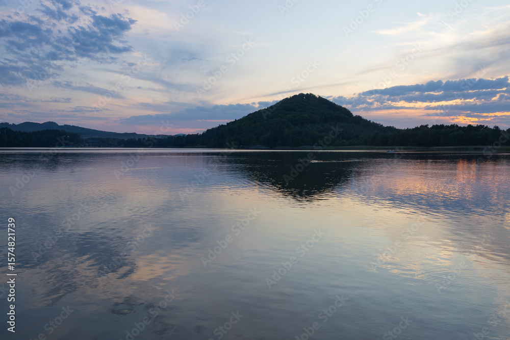 Fototapeta premium Tranquil lake and forested hill reflecting at sunset