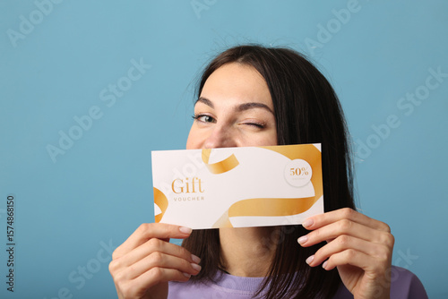 Joyful young brunette woman girl in yellow sweater posing isolated on pastel ,blue background studio portrait. People lifestyle concept. Mock up copy space. Hold gift certificate, doing winner gesture
