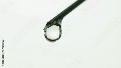 Slow motion footage of droplet falling from a syringe needle against a clean, sterile background