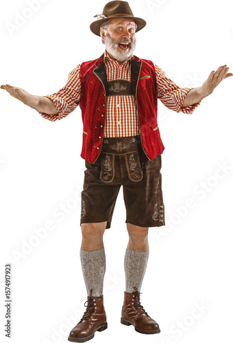 Obraz na plátně Senior man in traditional Bavarian costume with red vest brown lederhosen and hat standing against white background