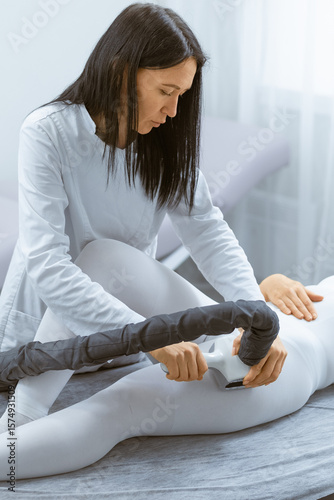 Woman calmly seated on massage table awaiting LPG massage treatment, wearing specialized treatment bodysuit