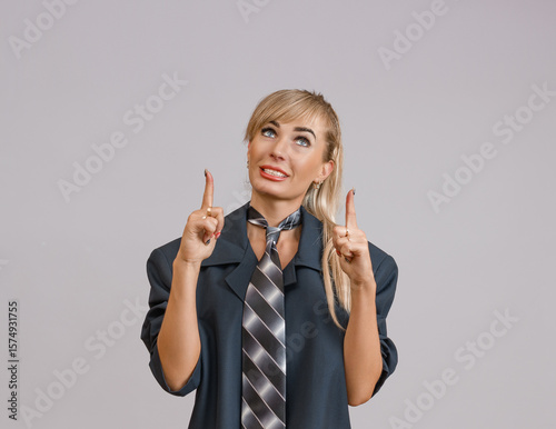 A woman in a dark suit and striped tie pointing upwards with both hands, looking optimistic and interested.