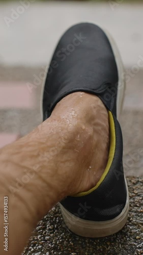 Vertical video. Man’s Wet Foot Wearing Black Shoe Resting on Rainy Steps During Tropical Downpour in Slow Motion, Contemplative Mood Concept