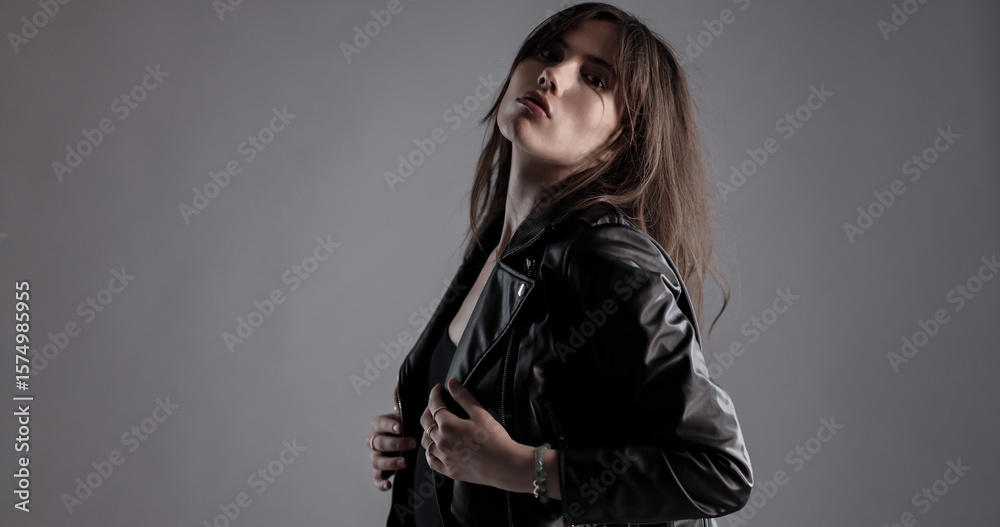 Fototapeta premium Fashion model wearing black leather jacket and posing in studio over gray background