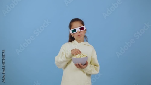 Child enjoys popcorn while wearing colorful 3D glasses in a bright blue setting creating a fun and playful atmosphere filled with excitement