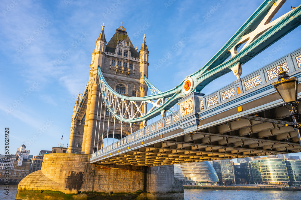 Obraz premium Early morning sunlight illuminates Tower Bridge, creating a stunning view over the Thames River. The iconic structure blends history with the vibrant atmosphere of London.