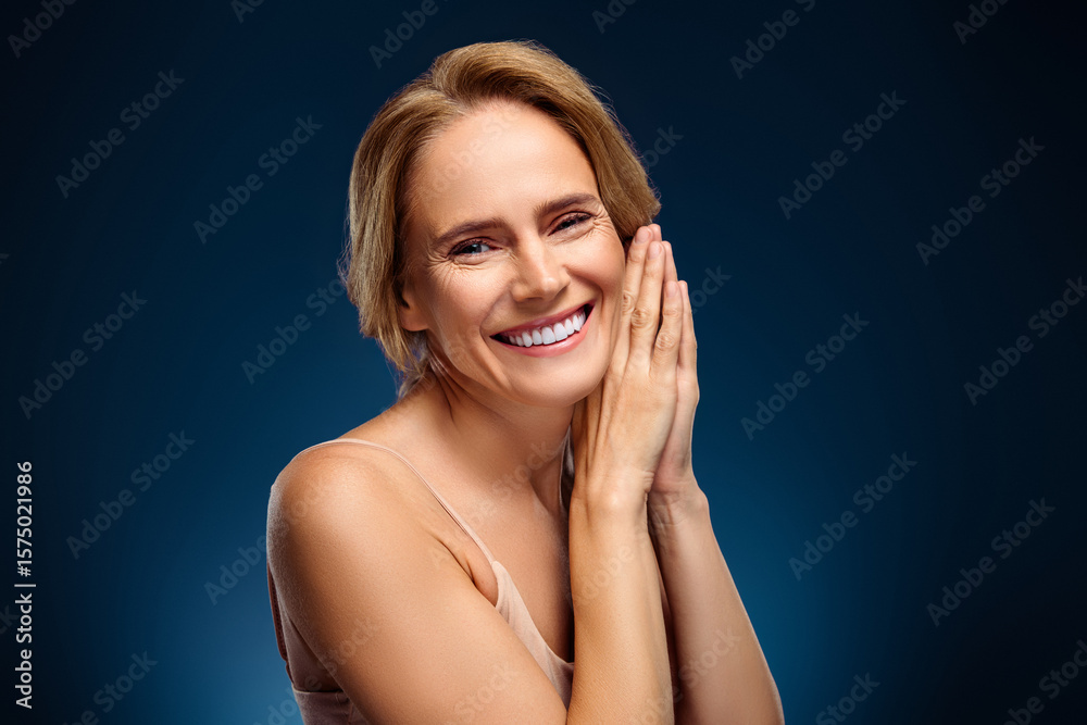 Fototapeta premium Smiling mature woman with glowing skin on a blue background, expressing positivity and charm