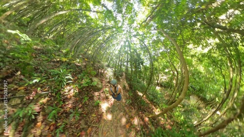 Woman continues hiking alone on jungle path under arched tropical trees in a warped spherical perspective, Digital Wilderness Concept