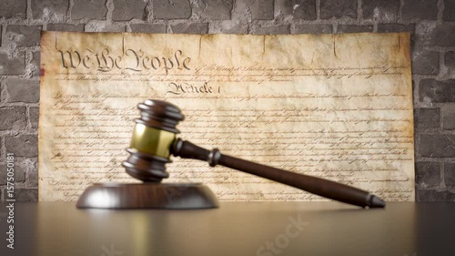 United States Constitution On Wall with Gavel Resting on Table in Front.