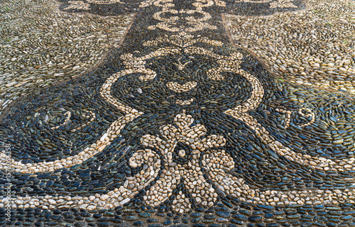 An old mosaic of cobblestone on the church square of S. Ambrogiy, Vrazzze in Italy, the Liguria region, the province of Savon. Liguria mosaic, rich in classic links, Palmettes, Menders