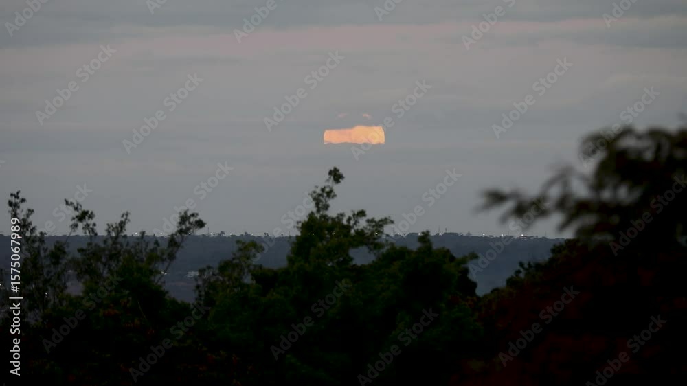 Video of the full moon rising moving through the gray clouds of a dramatic sky, birds flying past in the distance.