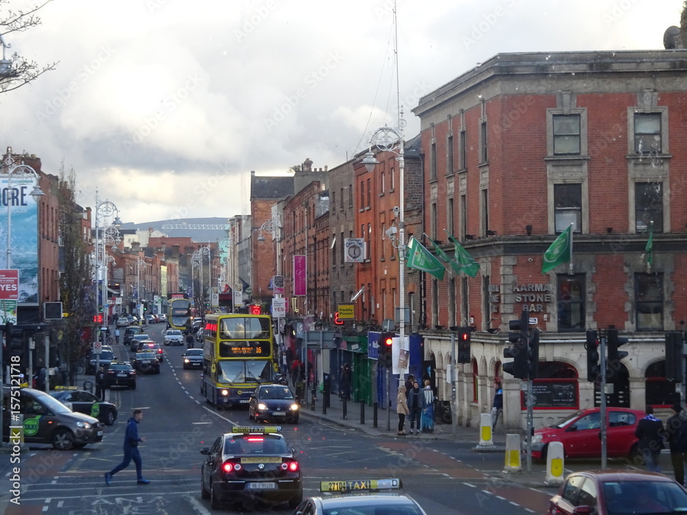 Fototapeta premium Red brick buildings and iconic Dublin buses on a lively main street with green flags