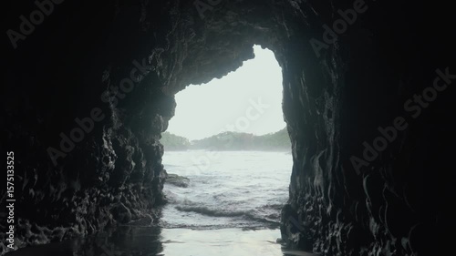 Wide shot of a sea cave opens to the ocean and distant land.