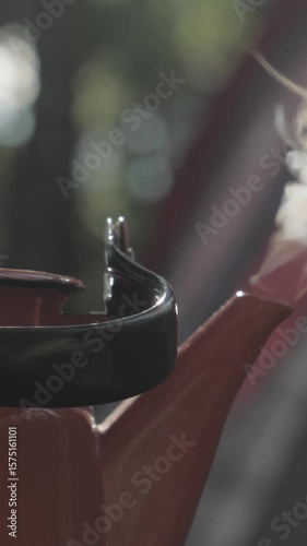 A holiday theme in nature. Steam rises from a red coffee pot. In the background a campsite in the summer forest. Defocused close-up shot. Vertical video.