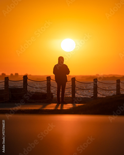 Photography Silhouette of a person watching the sunset at a lakeshore viewpoint