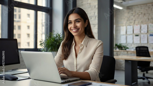 Busy young business woman executive using laptop in office. Smiling Hispanic businesswoman company employee sitting at work desk, professional female hr manager looking at pc computer at workplace.