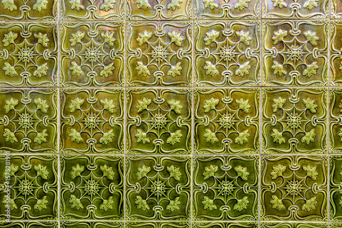 A panel of green tiles with embossed decoration covering a wall