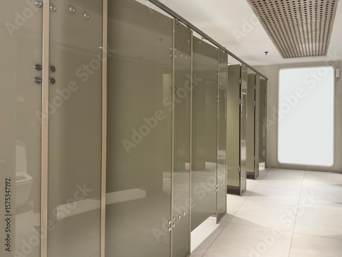 Public Restroom Stalls with Frosted Glass Doors and empty notice board mockup. Row of doors in Public toilet in Office Building or Mall.